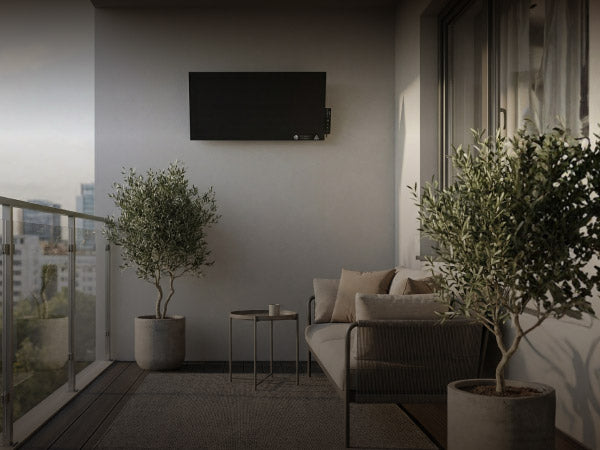 Schwarze Bringer Infrarotheizung an der Wand eines modernen Balkons montiert: Die Heizung sorgt im gemütlichen Ambiente mit Olivenbäumen und Lounge-Möbeln für Wärme.